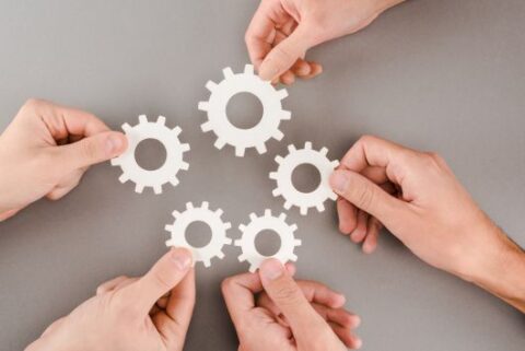 cropped view of people holding white gears on grey background
